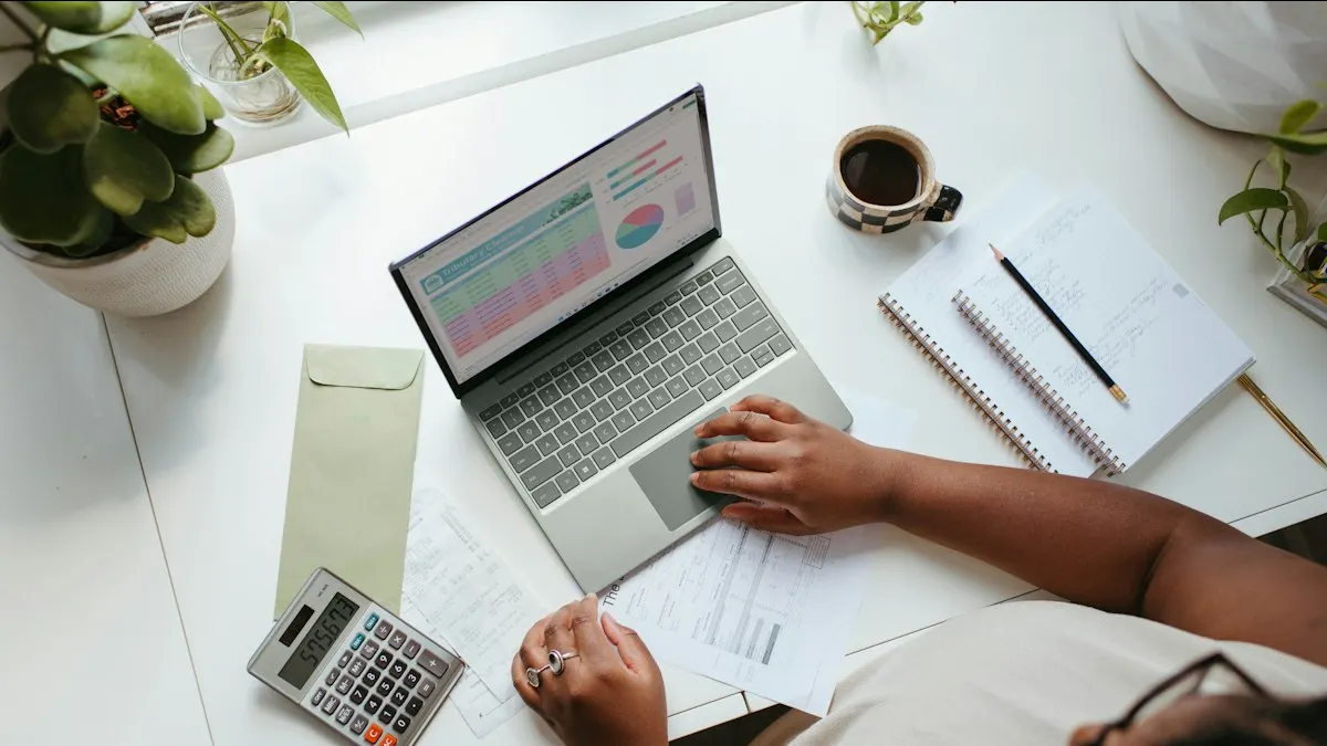 Pessoa sentada à mesa analisando gráficos de vendas na tela de um notebook, com anotações em papel ao lado